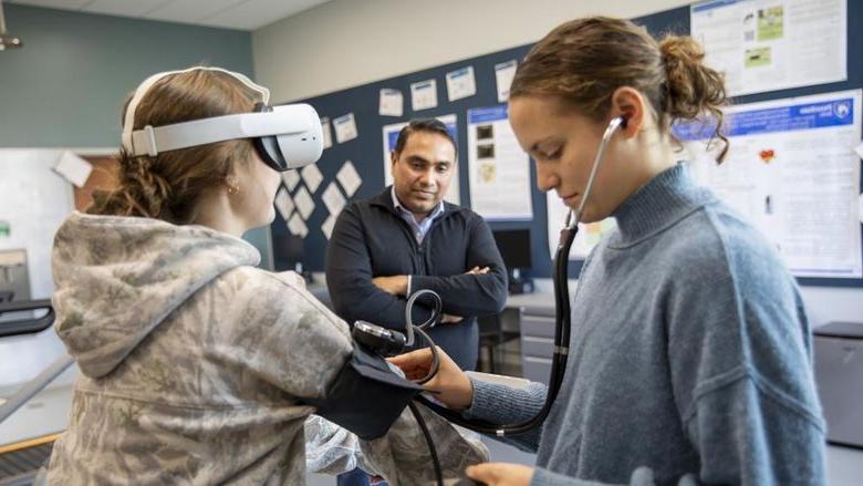 Student takes blood pressure of another student on stationary bike while faculty observes